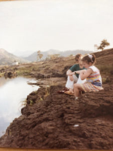 A woman and a girl sit by the side of a river